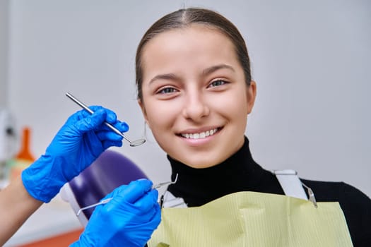 Teenage girl in dental chair with hands of dentist with tools