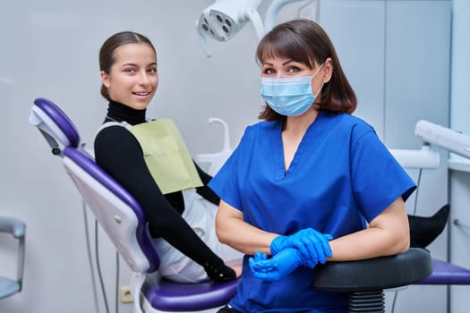 Portrait of female dentist looking at camera with young teenage girl patient sitting in dental chair. Dentistry, hygiene, treatment, medicine, specialist, career, dental health care concept