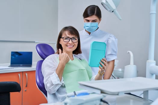 Woman patient together with dentist, patient sitting in dental chair looking at mirror