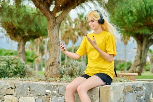 Hipster teenage girl in headphones with smartphone talking on video link