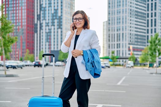Middle age business woman with suitcase, urban background.
