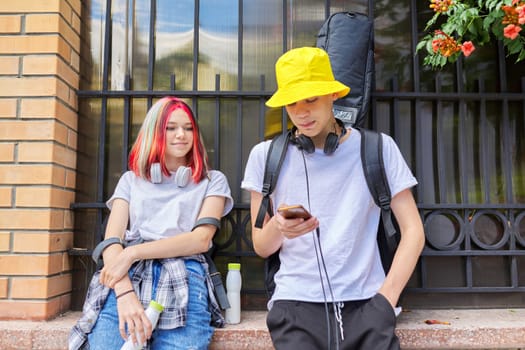 Couple of trending teenagers friends with smartphone on city street