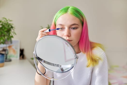 Teen girl with colored dyed hair dyeing eyelashes with mascara