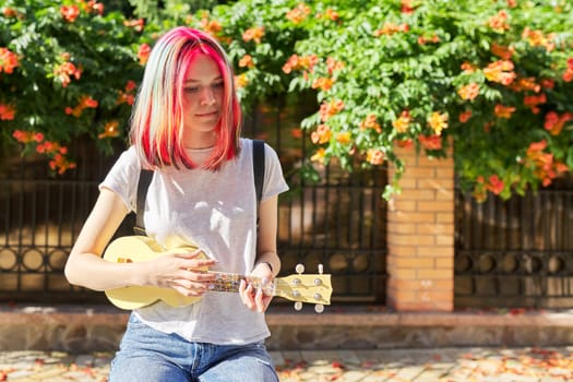 Hipster teenager playing ukulele sitting outdoors