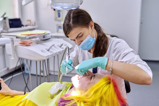 Female dentist treating teeth to patient, young woman in chair at dental clinic. Close-up view of real dental treatment of teenager girl, reportage photograph