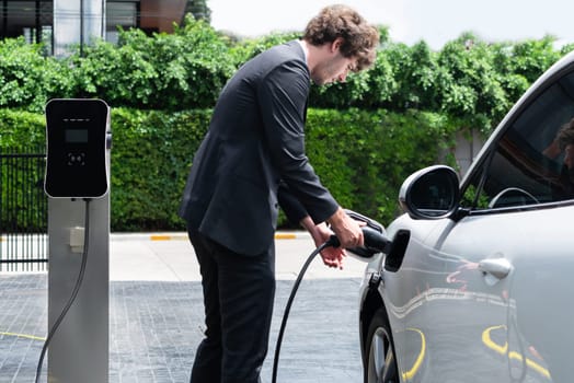 Progressive businessman charging EV car at public parking car charging station.