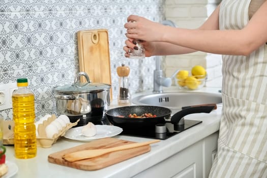 Young beautiful woman cooking at home in kitchen, fries eggs with sausages