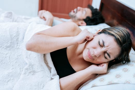 Wife suffering from her sleeping husband snoring. Sleep apnea concept, man snoring in bedroom and wife covering her ears