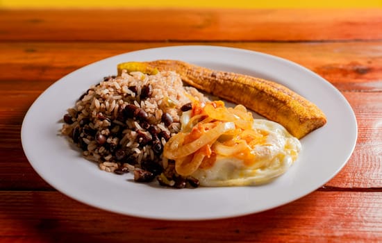 Gallopinto dish with ripe and fried eggs served on wooden table. Gallopinto breakfast with fried eggs and maduro on the table. Concept of typical foods of Latin America