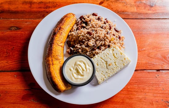 Gallopinto plate with cheese and maduro on wooden table. Nicaraguan food concept, Traditional Gallo Pinto meal with maduro and cheese served