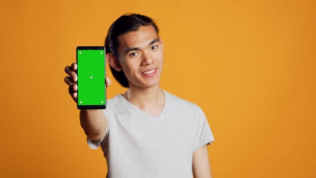 Cheerful young guy showing phone with greenscreen