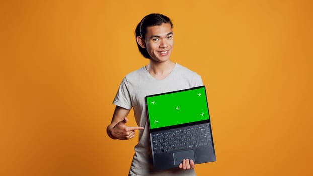 Cheerful man holding laptop with greenscreen on camera