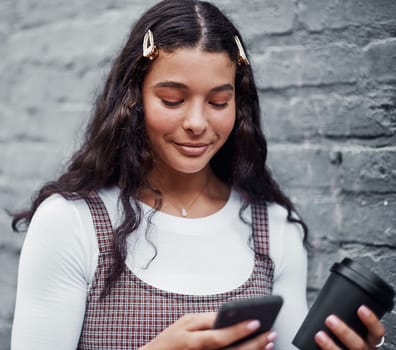 Coffee and technology go hand in hand. an attractive teenage girl standing alone and using her cellphone while holding a cup of coffee