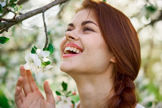 close portrait of a red-haired, laughing woman smelling flowers from a tree