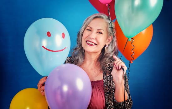 Balloons will always put a smile on my face. Portrait of a cheerful senior woman posing holding balloons in studio against a blue background.