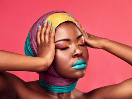 Capture this art, its rare. Studio shot of a beautiful young woman wearing a head wrap and make up against a pink background.