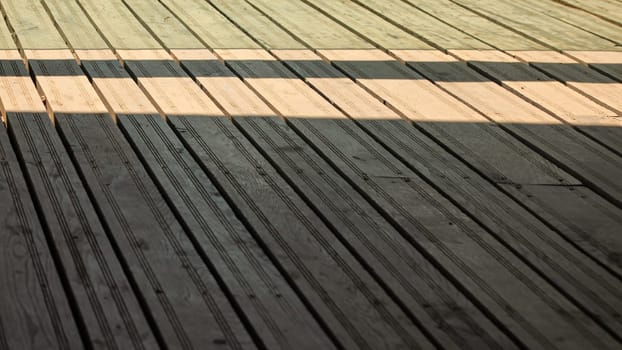 Regular exterior wooden board floor, sun casting shadow from side.
