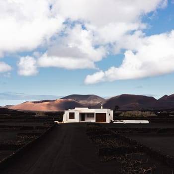 Traditional white house in black volcanic landscape of La Geria wine growing region with view of Timanfaya National Park in Lanzarote. Touristic attraction in Lanzarote island, Canary Islands, Spain.