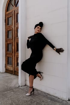 Stylish woman in the city. Fashion photo of a beautiful model in an elegant black dress posing against the backdrop of a building on a city street