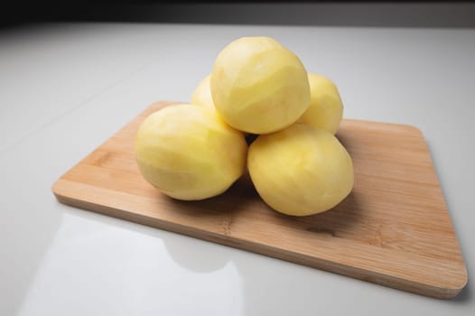 pile of peeled potatoes on a wooden cutting board. Clean potatoes on the table. Cook food, peel potatoes