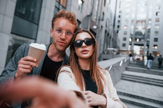 Makes selfie. Woman and man in the town at daytime. Well dressed people