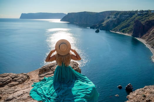 Woman sea. A happy girl is sitting with her back to the viewer in a mint dress on top of a mountain against the background of the ocean and rocks in the sea.