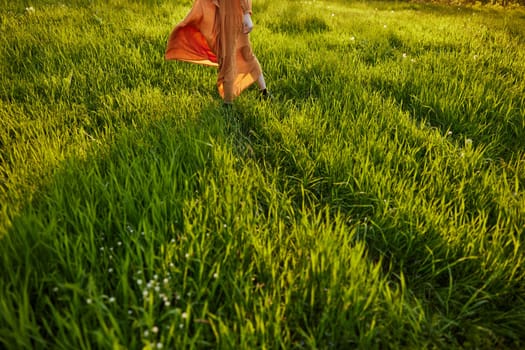 horizontal photo of a woman in an orange dress photographed without a face, standing in a green field during sunset, illuminated from the back
