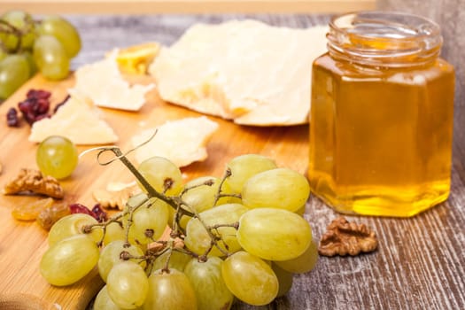 Different type of cheese, honey and grape on wooden background