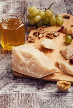 Big piece of parmesan next to nuts, grape and honey