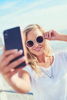 Put on your shades and snap it. a young woman taking a selfie while spending the day by the sea.