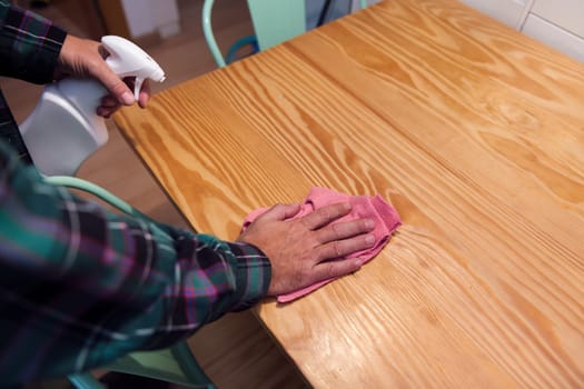 person cleaning a table with a rag and a spray