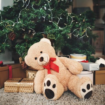 Christmas, gift and festive with a teddy bear by a tree, ready for celebration during the holiday season. December, event and a stuffed animal sitting in the living room of an apartment as a present.