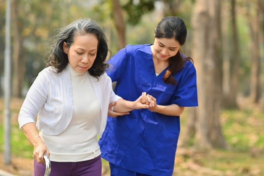 Female medical worker helping senior woman walking in rehabilitation park. Assistance and rehabilitation concept