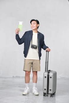A satisfied young man looking camera holding passport and tickets isolated over white background