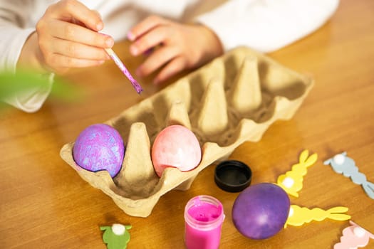 Close up of child hands painting Easter eggs on wooden table. Happy Easter. Preparation for Easter.