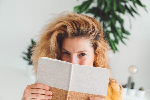 Playful blonde woman hiding half of her face behind a note book