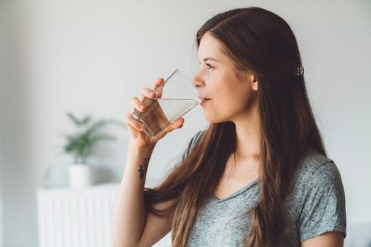 Waist up side portrait young brunette drinking a glass of water on white background
