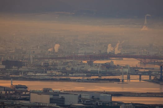 Smoke mixes with atmospheric haze along industrial riverside at dawn