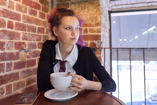 Teen schoolgirl sitting in cafe with cup of cappuccino