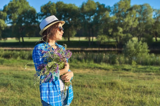 Country portrait of an adult beautiful woman in hat with bouquet of wildflowers