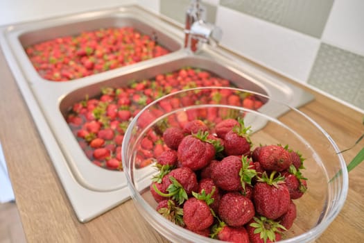 Strawberry season, washing berries in water in wash basin at home kitchen