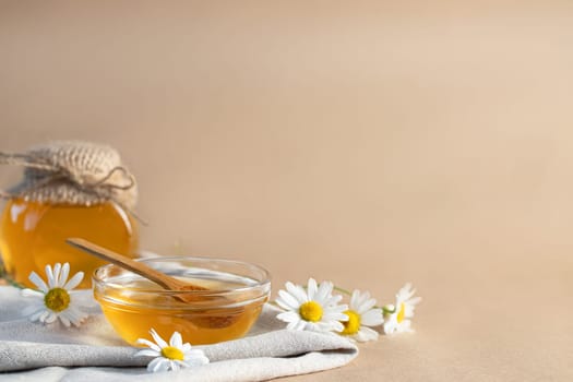 Chamomile syrup in a small bowl and in a jar and chamomile flowers on a linen kitchen towel, copy space