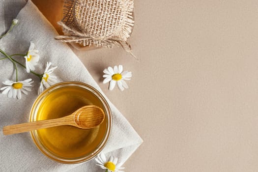 Chamomile syrup in a small bowl and in a jar and chamomile flowers on a linen kitchen towel, topview, copy space