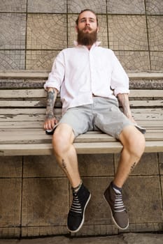 Bearded tattooed hipster lying on a bench