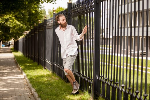 Bearded hipster posing next to a fence
