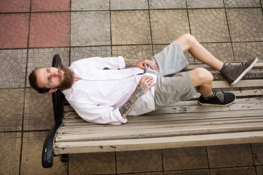 Bearded hipster lying on a bench