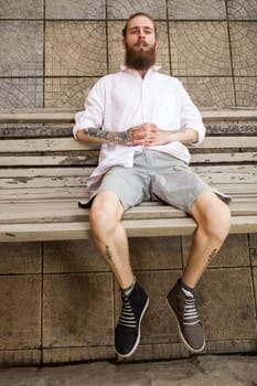 Bearded tattooed hipster lying on a bench