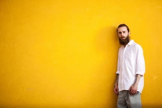 Tattooed fashion bearded hipster on yellow wall posing outdoor