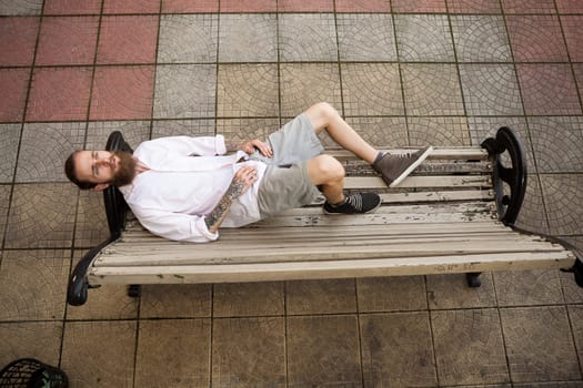 Cool bearded hipster lying on a bench