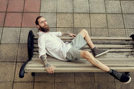 Bearded tattooed lying on chair and posing in fashion style. Nonconformism and hipster